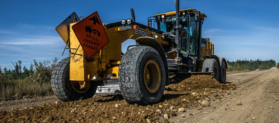 Two John Deere motor graders parked beside each other on a dirt road.